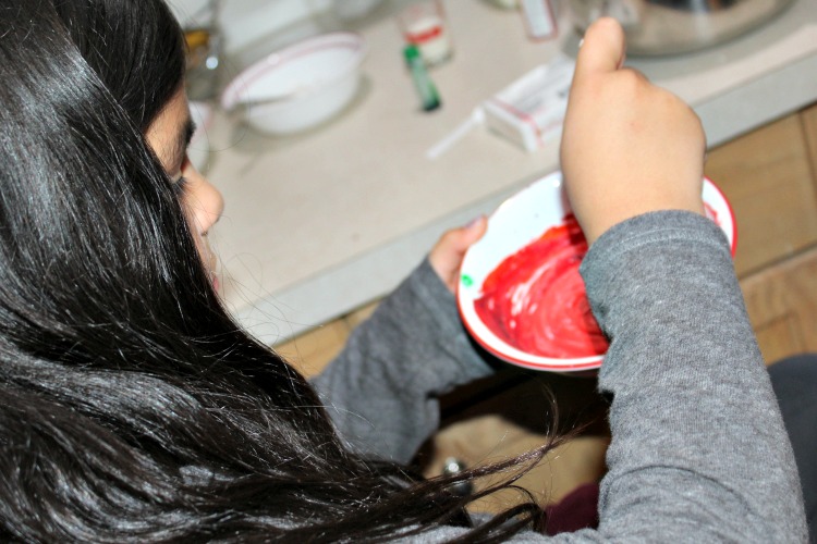 Isabella making colored frosting in a bowl 