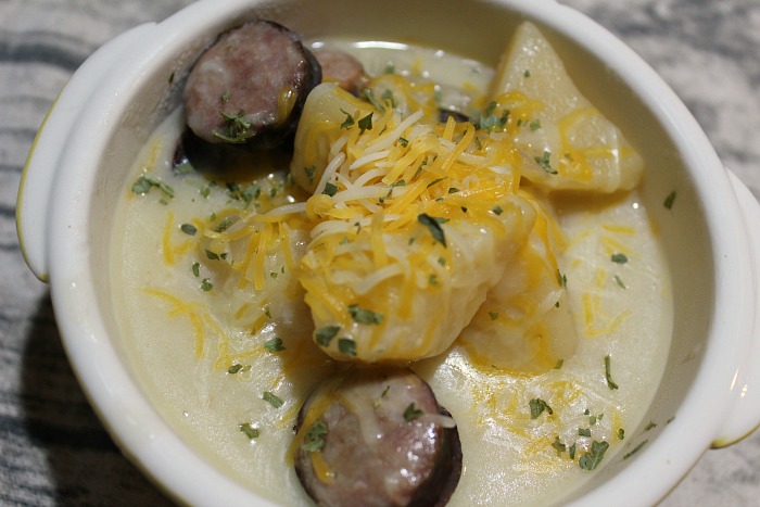 crockpot potato sausage soup served with cheese on top in a white bowl