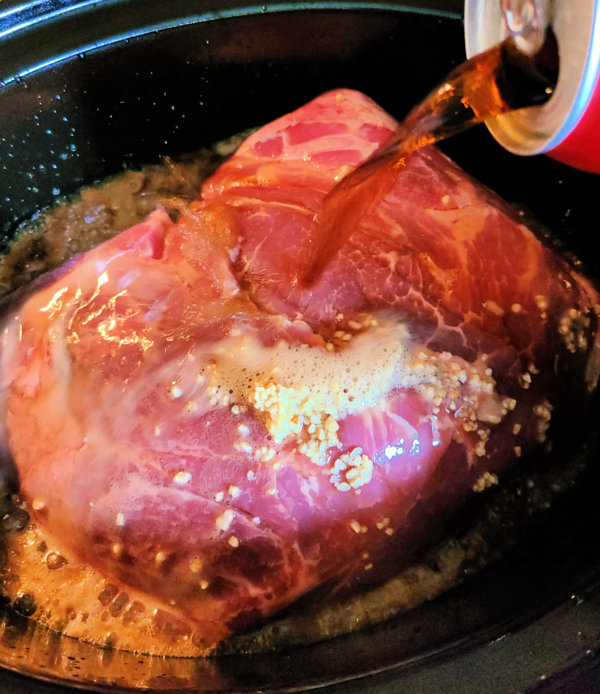 Pork shoulder roast with coca cola being poured over it in a crockpot 