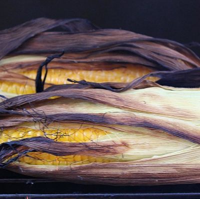Grilled corn on the cob in a husk on the grill cooking