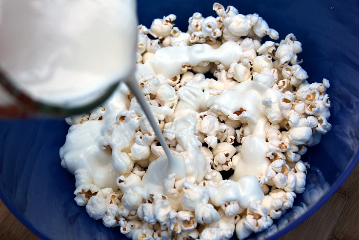 Melted white almond bark being poured over popped popcorn