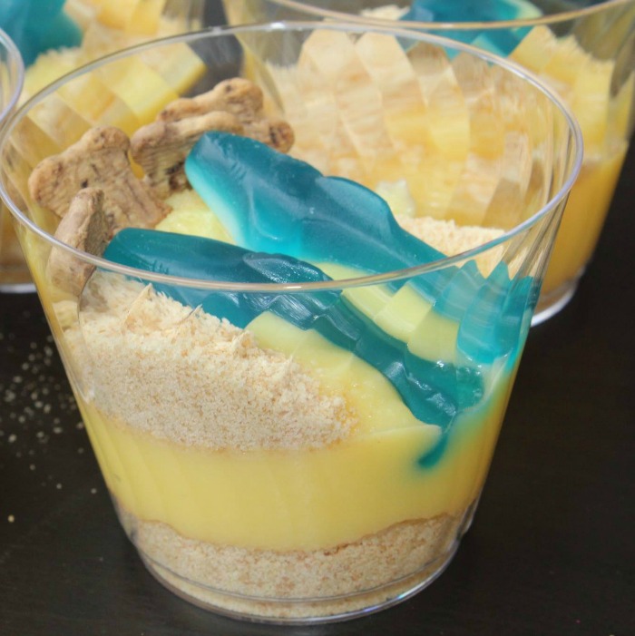 Sand cups assembled with ground vanilla wafers, with vanlla pudding with more sprinkled vanilla wafers with shark gummies in it 