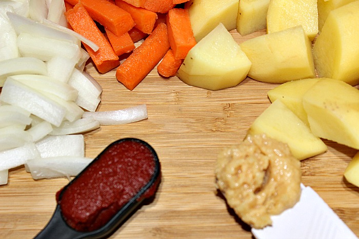 Gold Potatoes, cut carrot Sticks, chopped onions, tomato past, and minced garli on cutting board