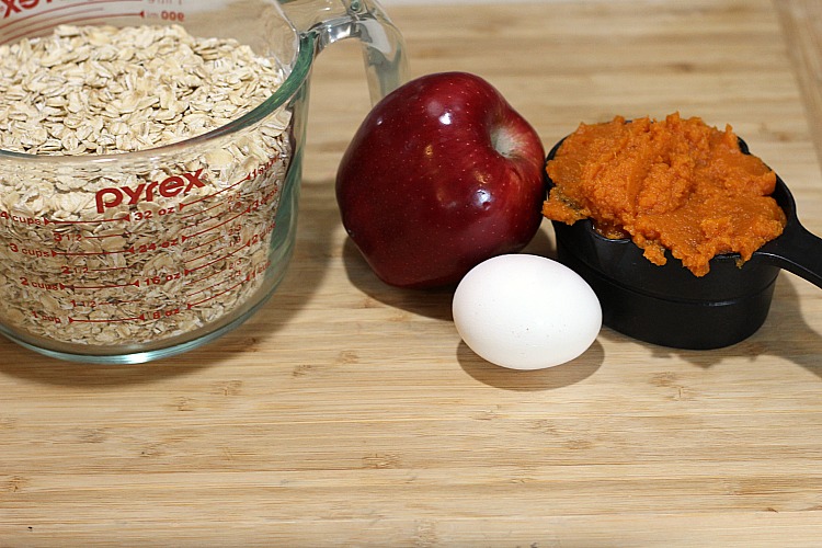 Canned pumpkin, a small apple, an egg, and oats in a measuring cup on a cutting board