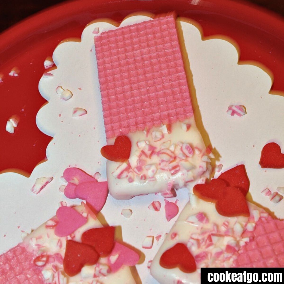 Pink wafer cookies dipped in white chocolate sprinkled with sprinkles on a red plate 