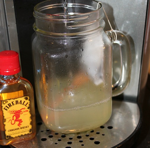 Water brewing into Lemon Juice, honey, and tea bag in a mason jar glass on a Keurig maker next to a shot of fireball.  