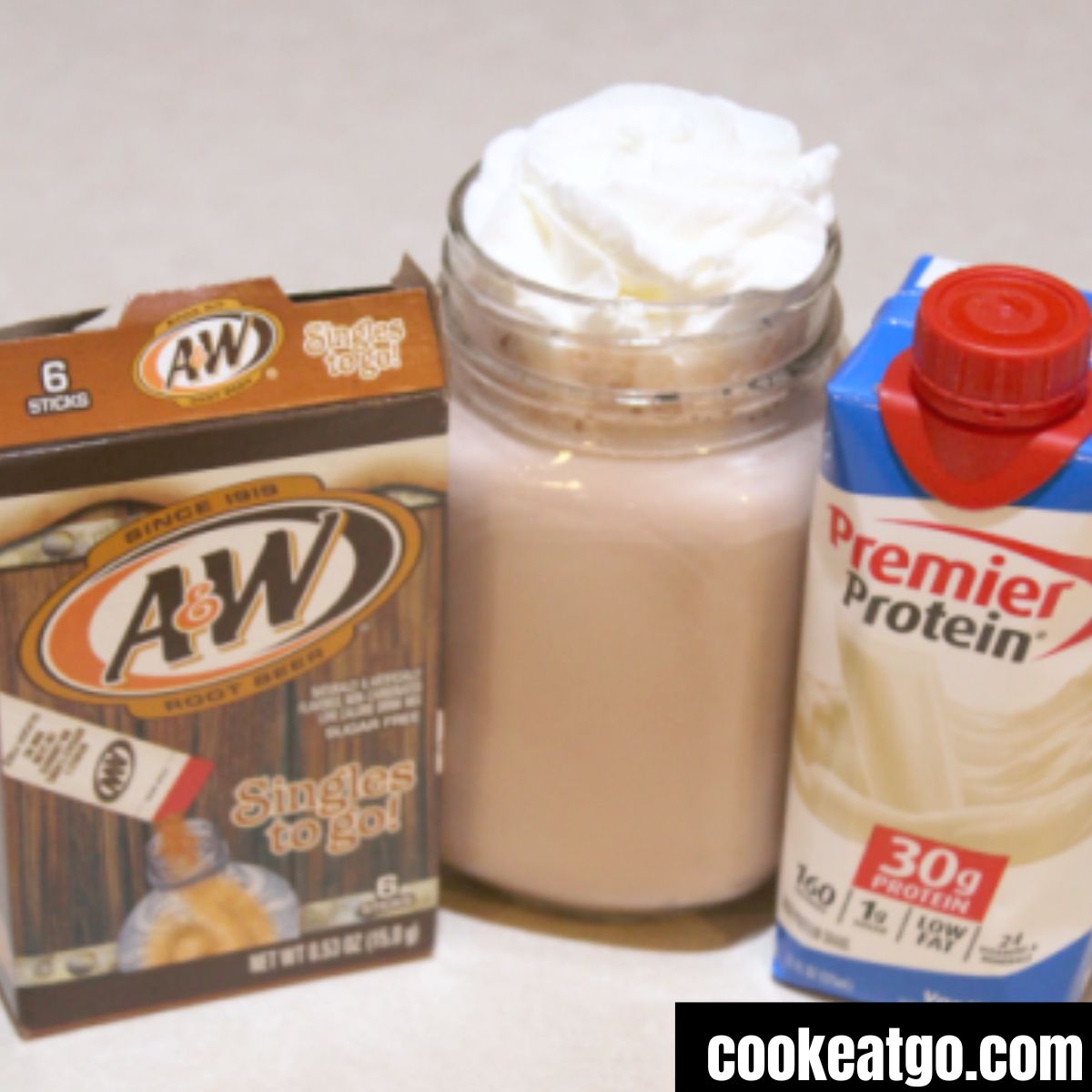 Premier Protein Rootbeer float in a mason jar glass topped with whipped topping next to a premier protein vanilla and a box of root beer powder 