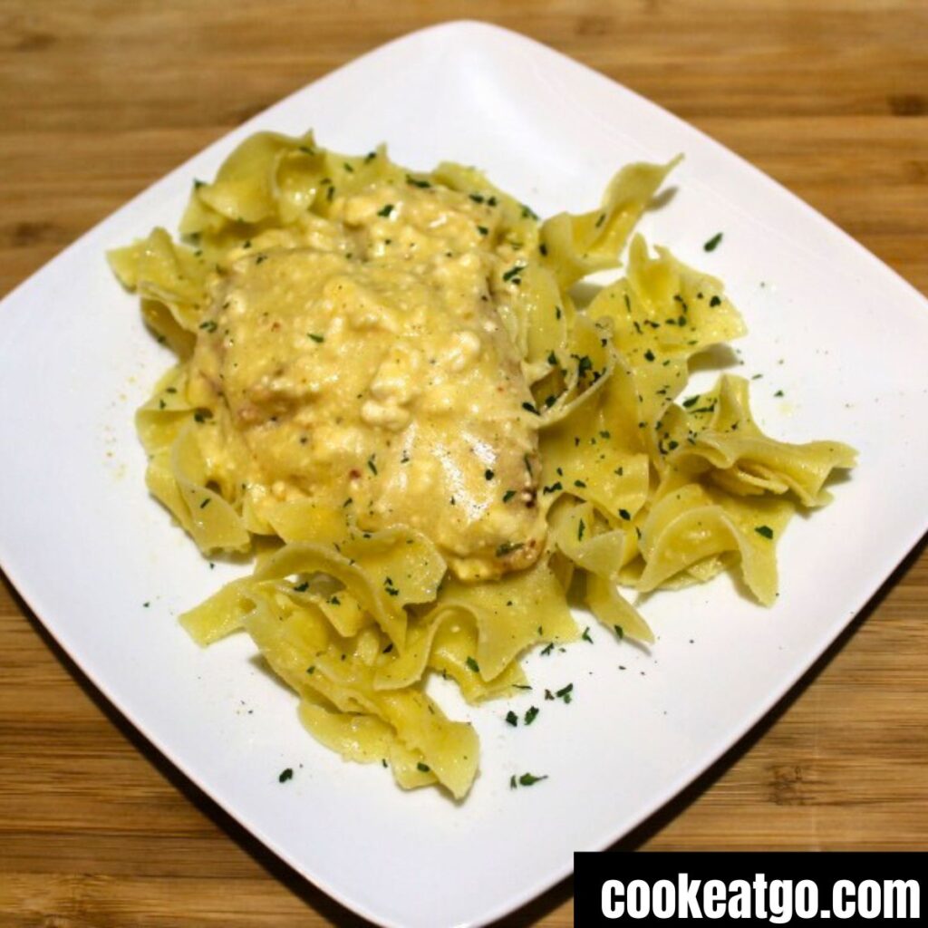 Cream cheese chicken served over a bed or egg noodles on a white plate