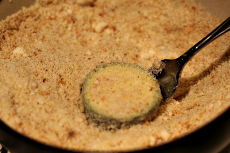 Sliced zucchini dipped in egg wash being dipped in bread crumbs 