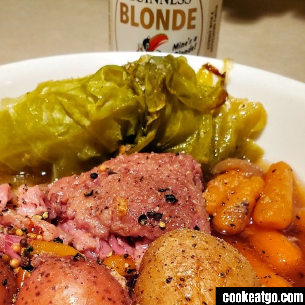 guinness corned beef and cabbage dutch oven served in bowl with bottle of beer behind it