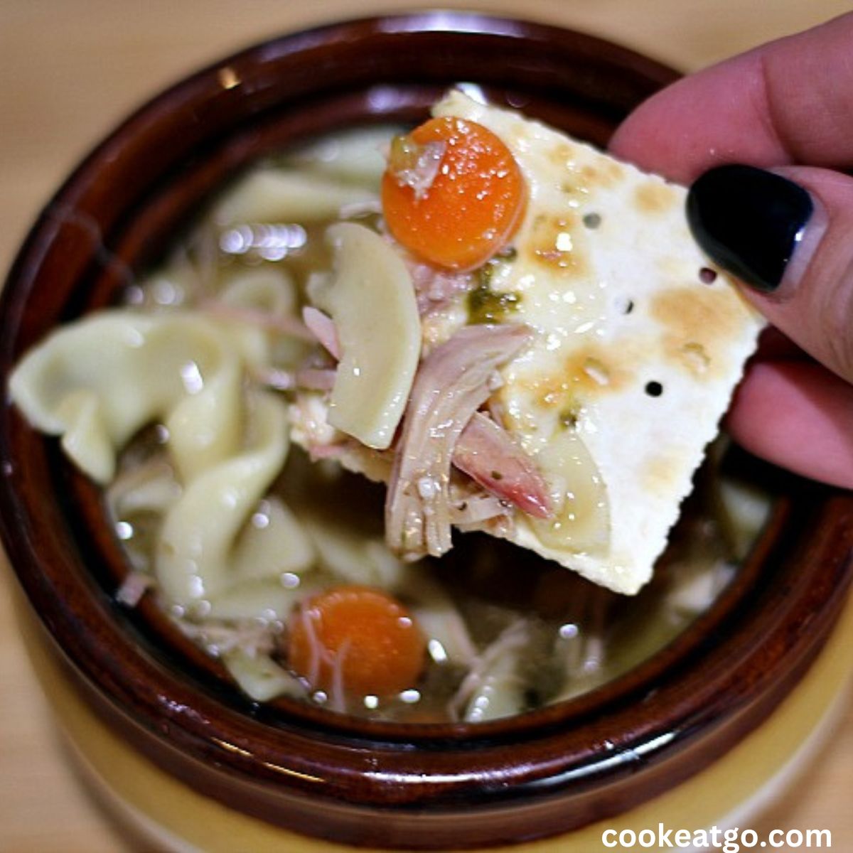 Smoked Turkey Noodle Soup in a soup crock with soup on a saltine