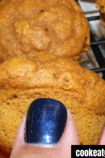 Thumb holding a pumpkin weight watchers muffin with a baking rack covered in 3 ingredient pumpkin muffins behind it