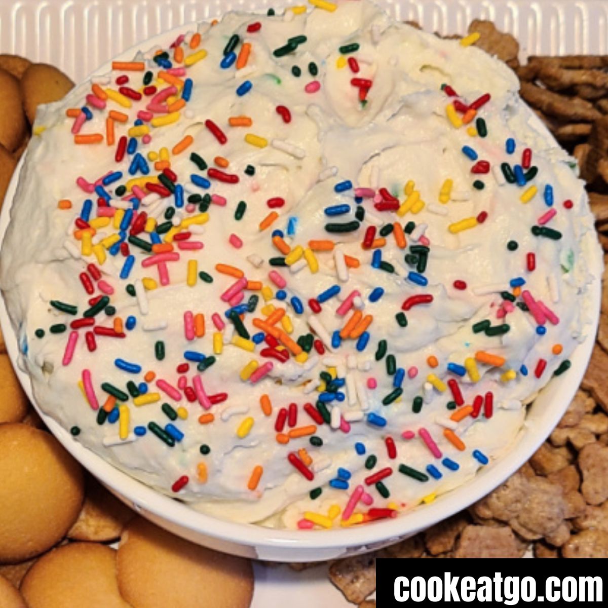 Funfetti cake dip served in a bowl with vanilla wafers and teddy grahams