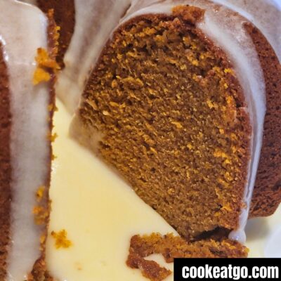 Pumpkin bundt cake with a slice missing with a pool of cream cheese frosting