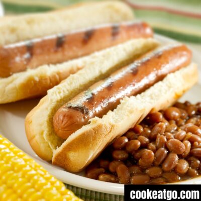 Hot dogs served on a plate wtih beans and an ear of corn