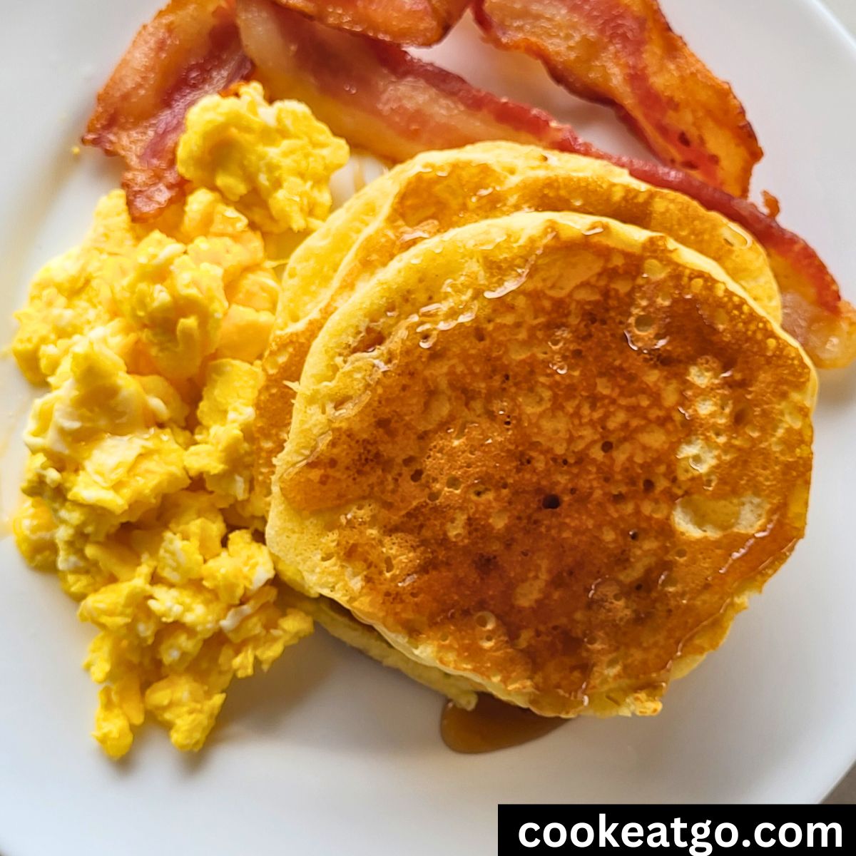 fluffy pancakes topped with syrup served with eggs and cooked bacon on a plate