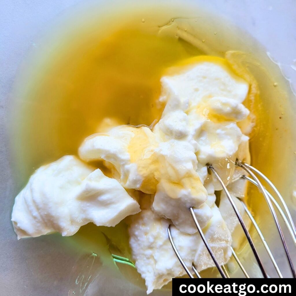 Ingredients for creamy dressing for weight watchers coleslaw in a bowl with a metal whisk, greek yogurt, apple cider vinegar, and honey