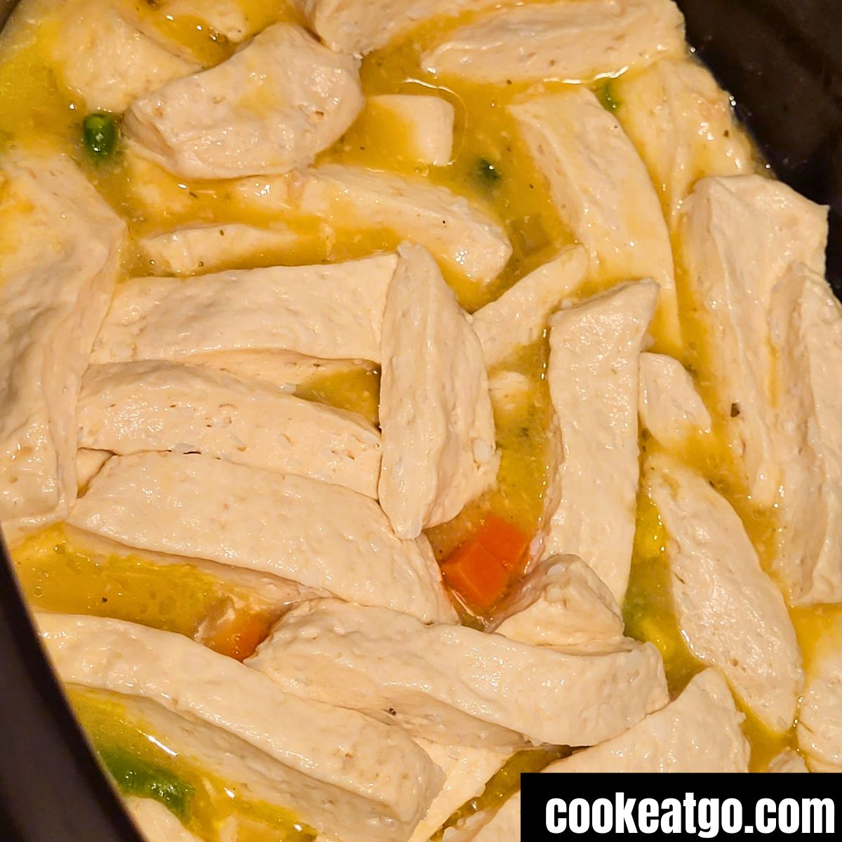 Sliced refrigerator biscuit in crockpot of chicken and dumpling before biscuits cooking