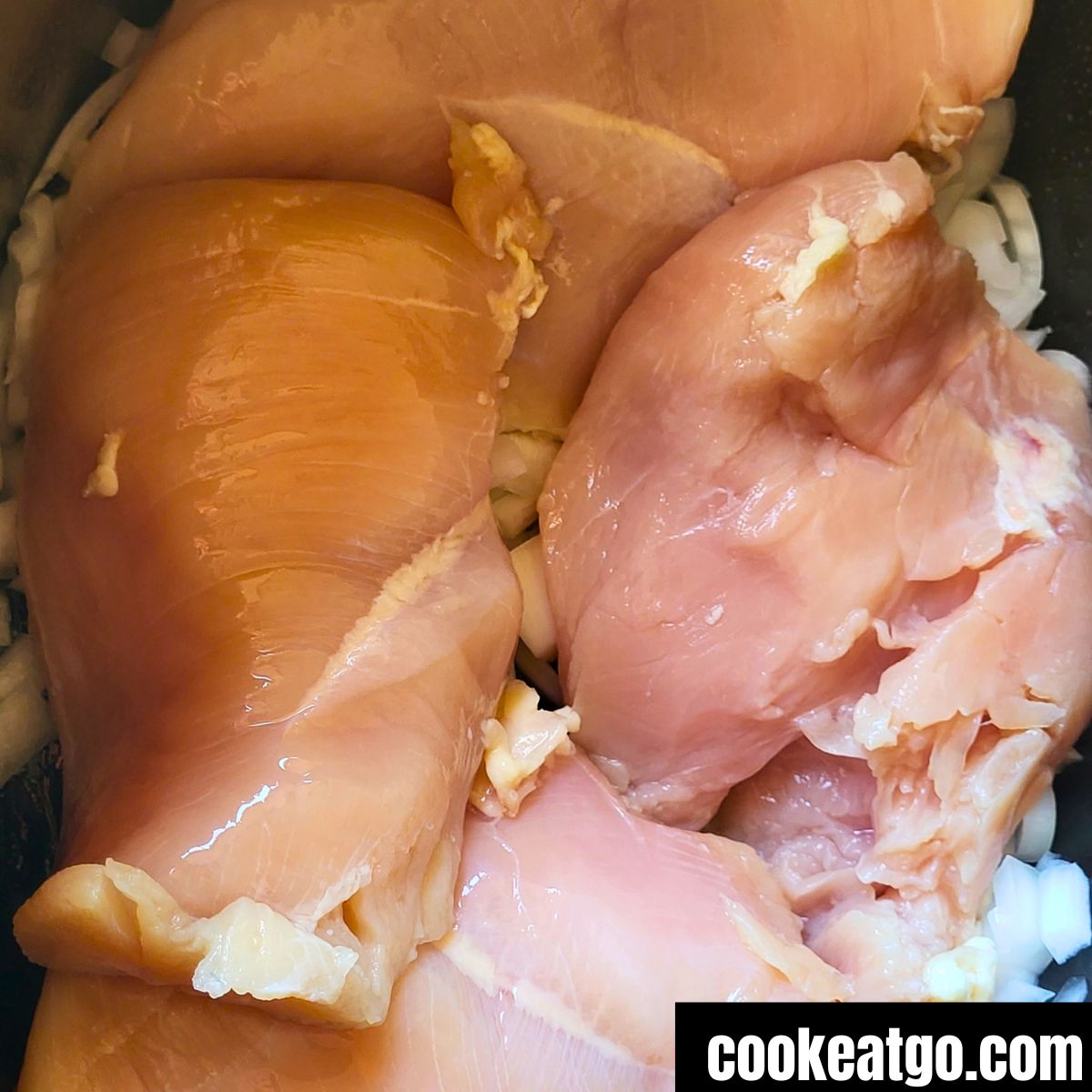 Raw chicken breasts on white onion in crockpot for chicken and dumpling