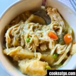 White bowl of crockpot chicken and dumplings with a spoon in it