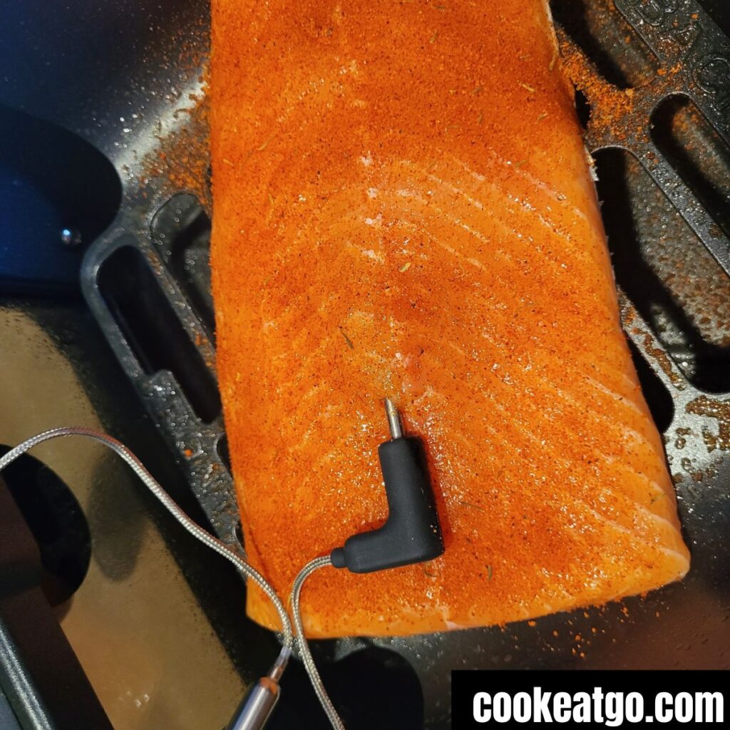 Salmon fillet seasoned with rub in air fryer basket with temperature probe in fillet