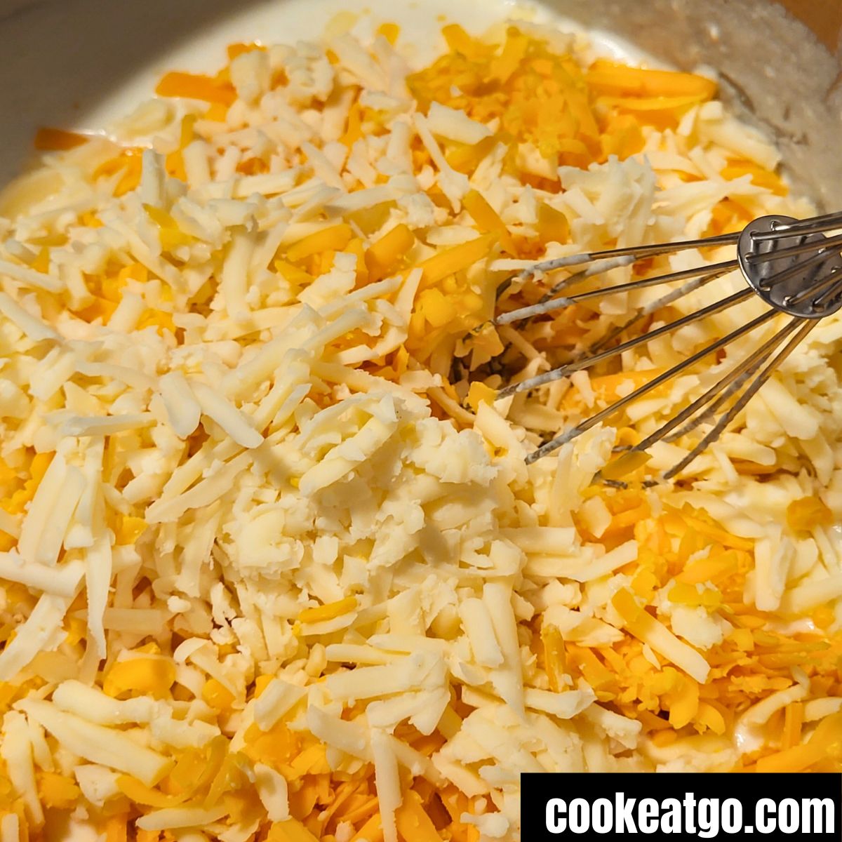 Shredded cheese melting into cream cheese milk mixture in a pot