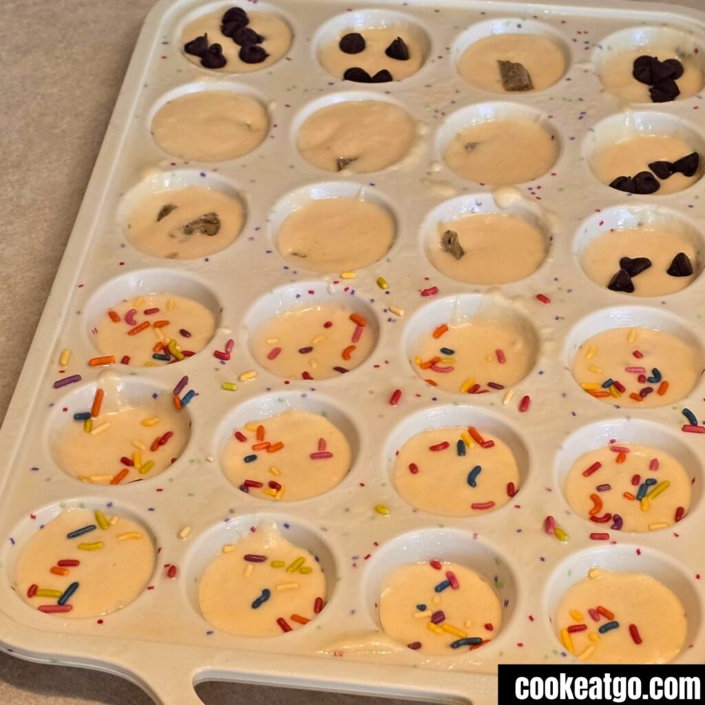 Panckae Batter In Mini Muffin Pan topped with sprinkles, sausage, and chocolate Chips